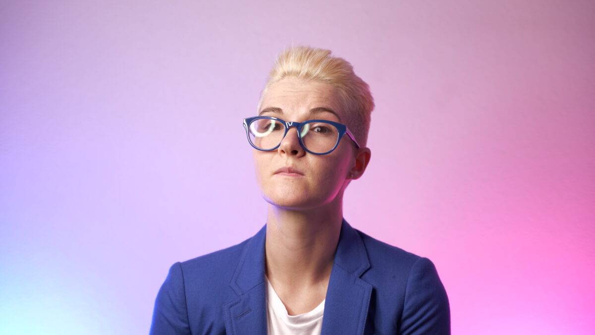 portrait of Tracy in blue glasses and a blue blazer against a blue and pink gradient